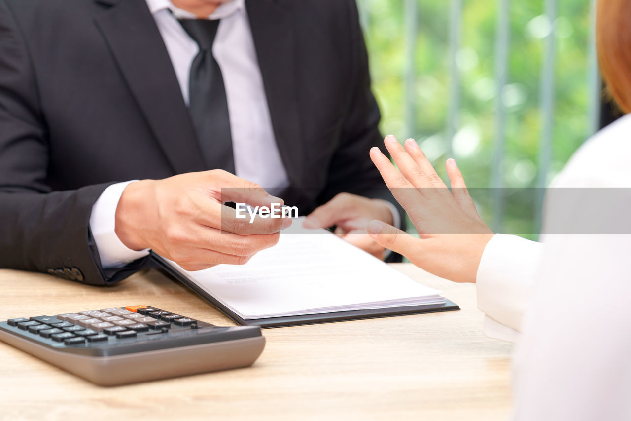 Cropped image of businesswoman gesturing stop sign for signing on contract at table in office