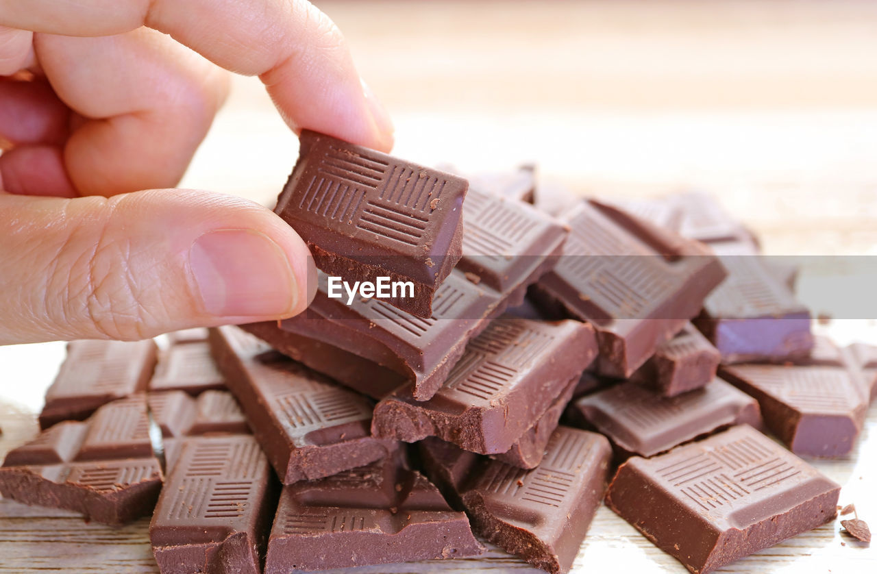 Closeup man's fingers picking a chunk of chocolate from its pile