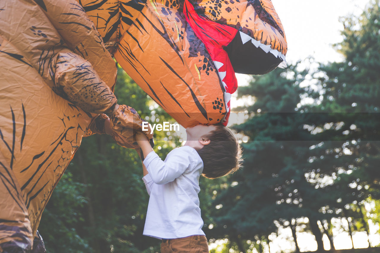 Boy kissing person wearing dinosaur costume in park