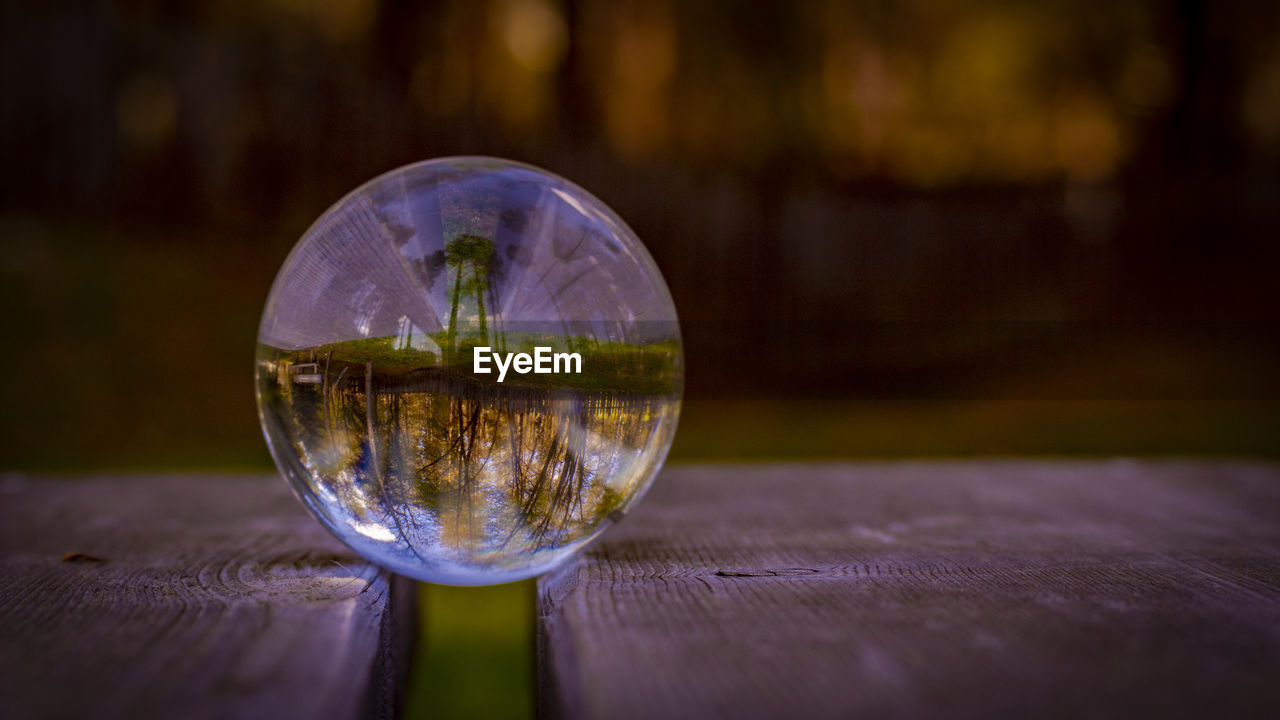 reflection, water, macro photography, yellow, glass, light, close-up, wood, sphere, nature, no people, transparent, green, outdoors, table, crystal ball, focus on foreground, blue, plant, darkness, lighting, environment, leaf, single object, tree, selective focus, night, shape, geometric shape