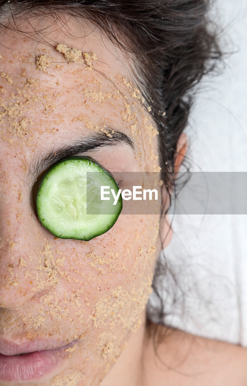 Close-up of woman with facial mask and cucumber 