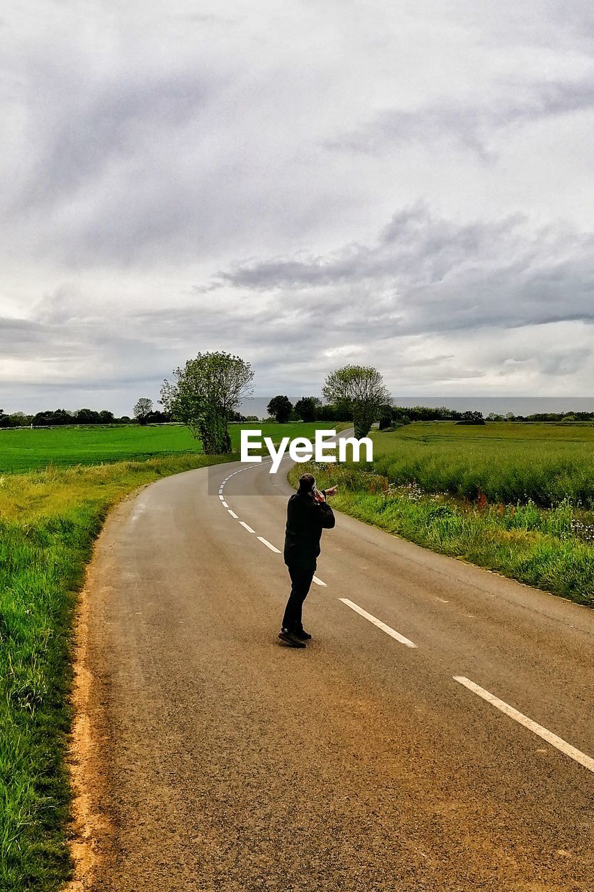 MAN CYCLING ON ROAD AGAINST SKY