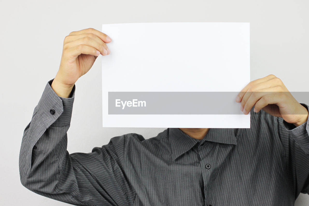 Close-up of businessman holding blank paper against white background