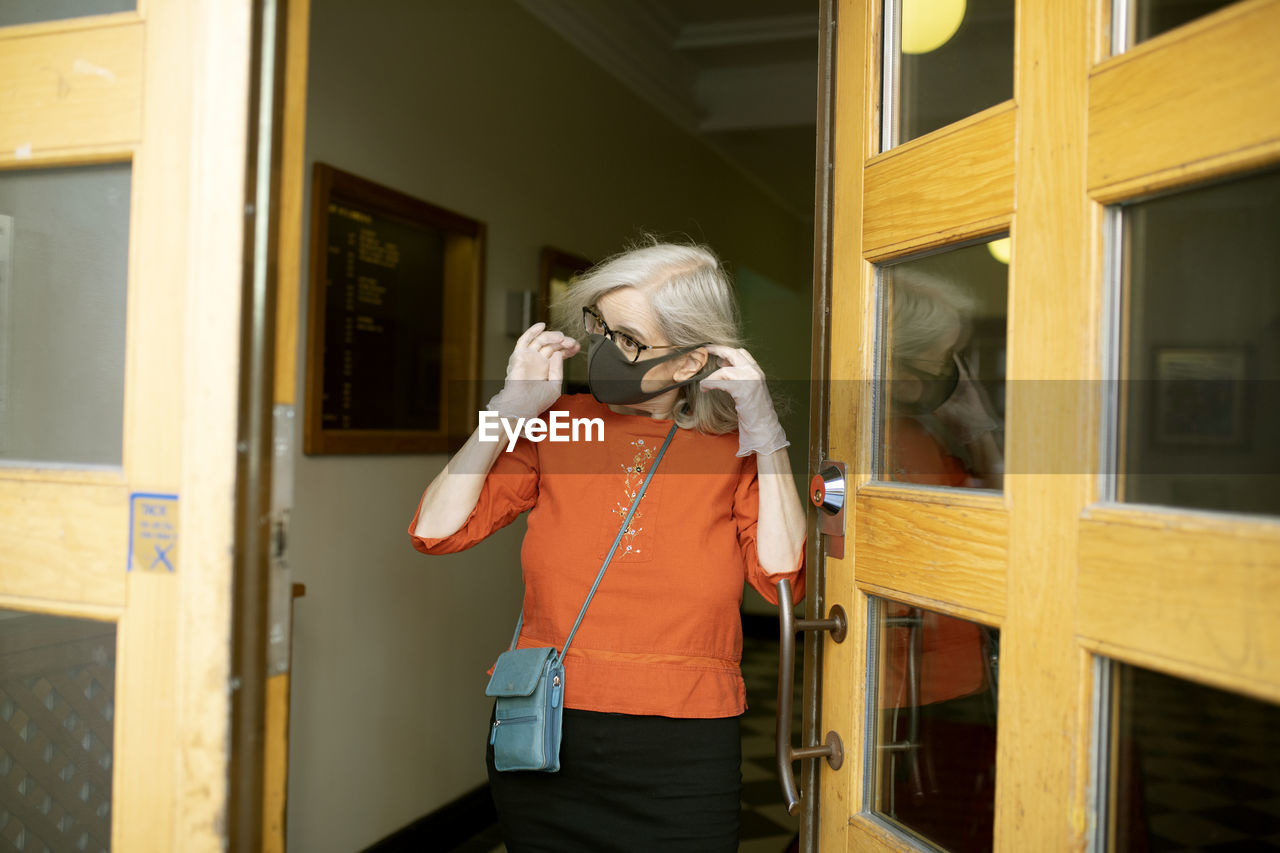 Woman putting face mask on while leaving house