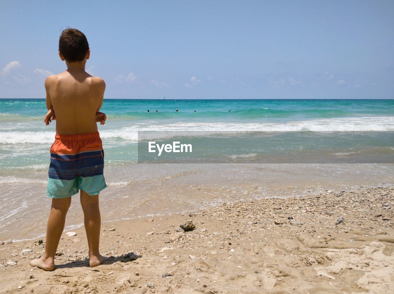 Shirtless boy standing at beach against sky