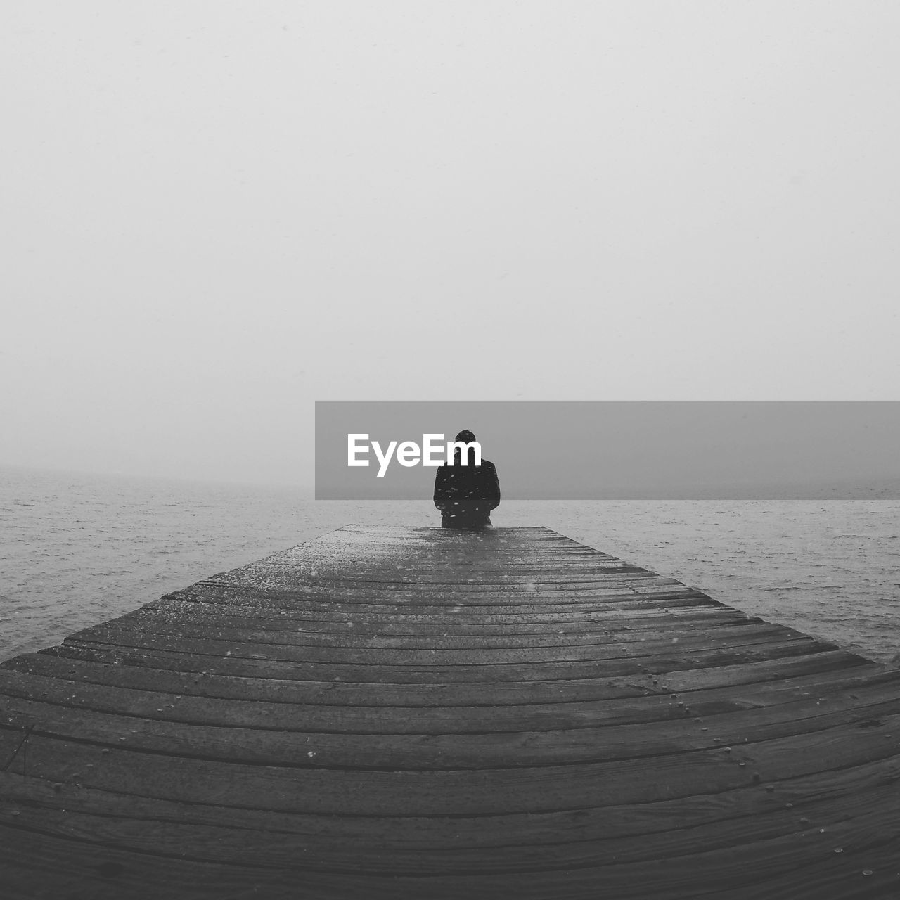 Man sitting on pier looking at sea