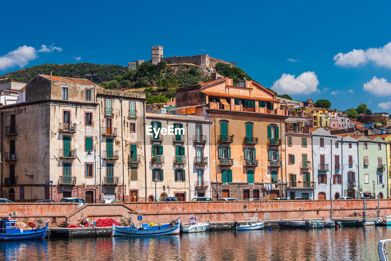 Boats moored on river by buildings in city against sky