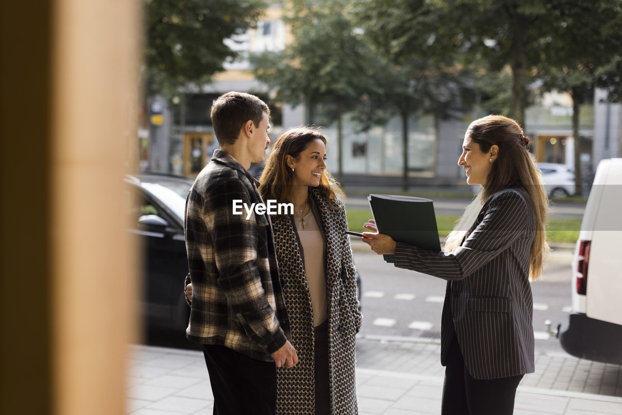 Smiling saleswoman talking with couple while standing at street