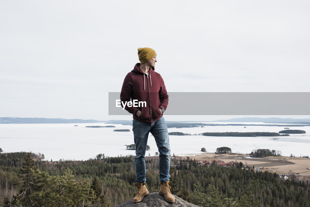 Man standing on a rock whilst hiking a hill above the ocean in sweden