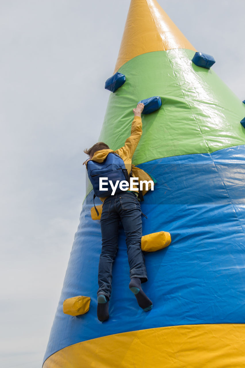 Rear view of person climbing on bouncing castle against sky