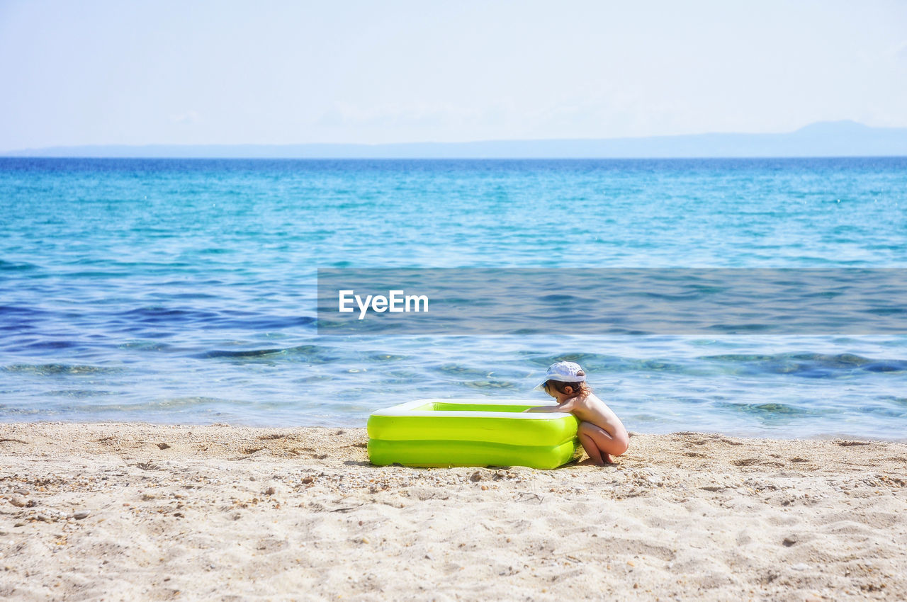 Side view of naked boy by wading pool on shore at beach against sky