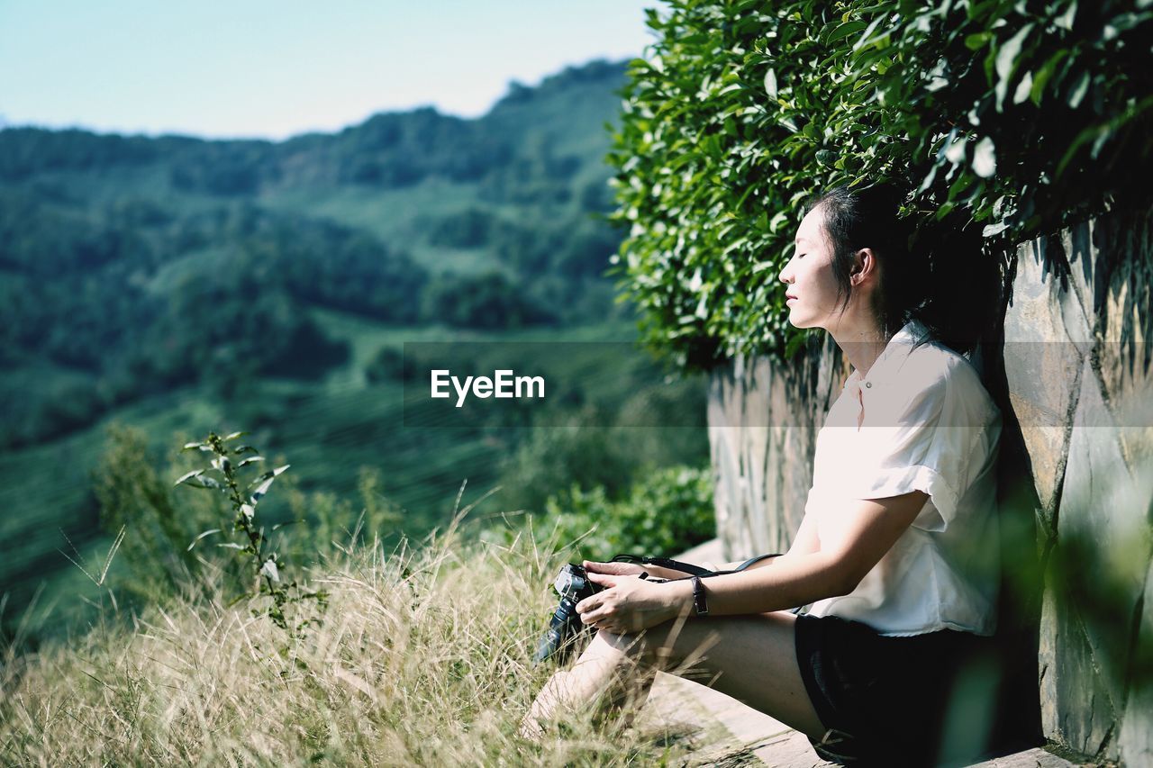 Side view of woman sitting on by wall on mountain