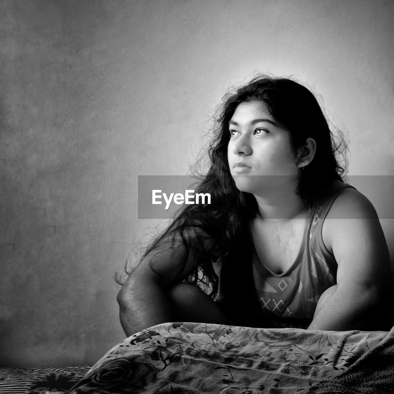 PORTRAIT OF WOMAN SITTING ON BED AGAINST WALL