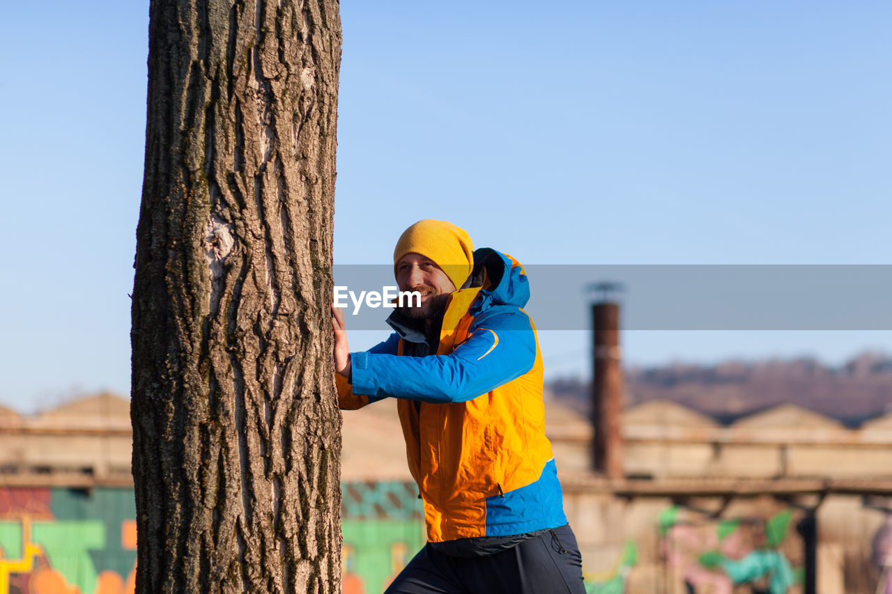 Portrait of mid adult man standing by tree against clear sky