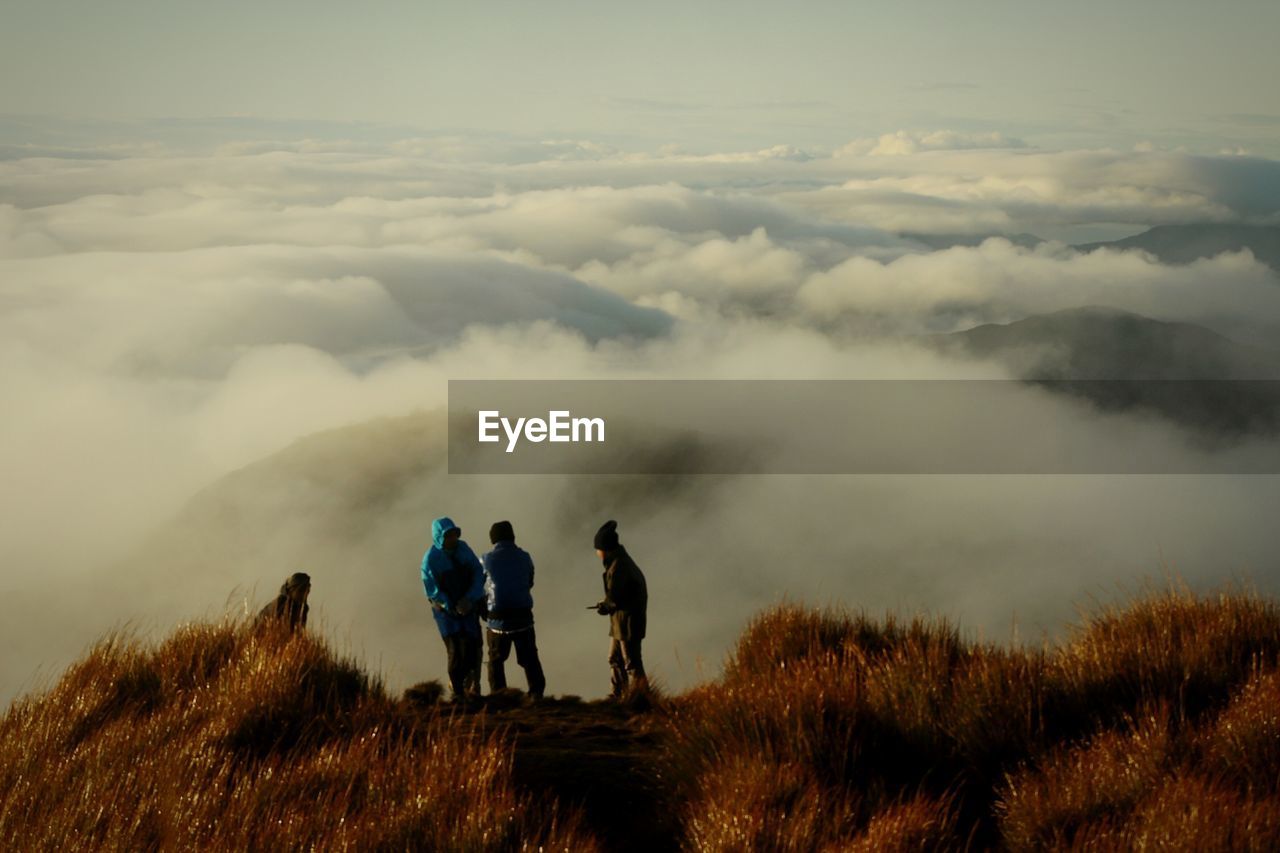 Hikers standing on mountain by cloudscape against sky