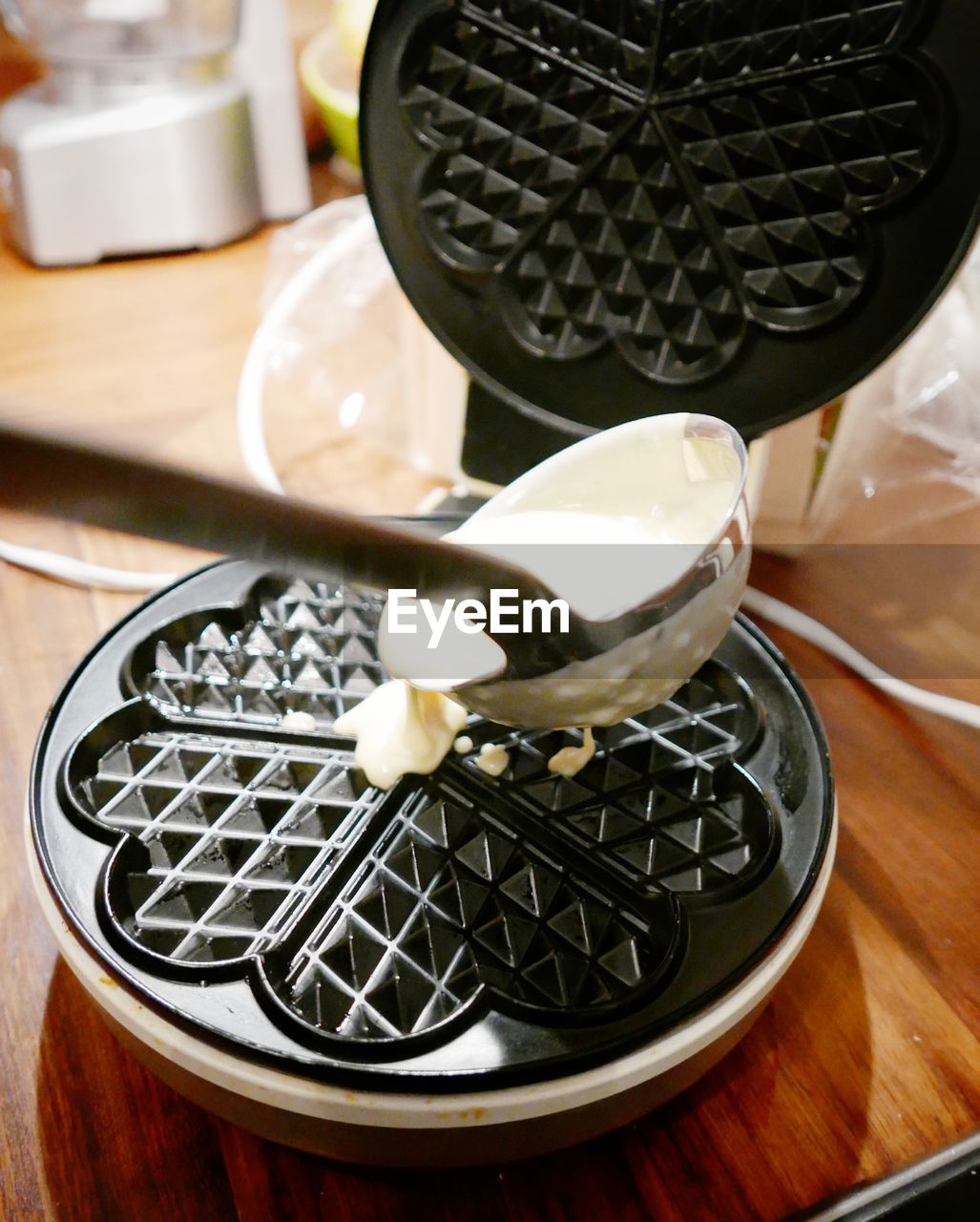 Close-up of spoon with batter pouring on waffle iron