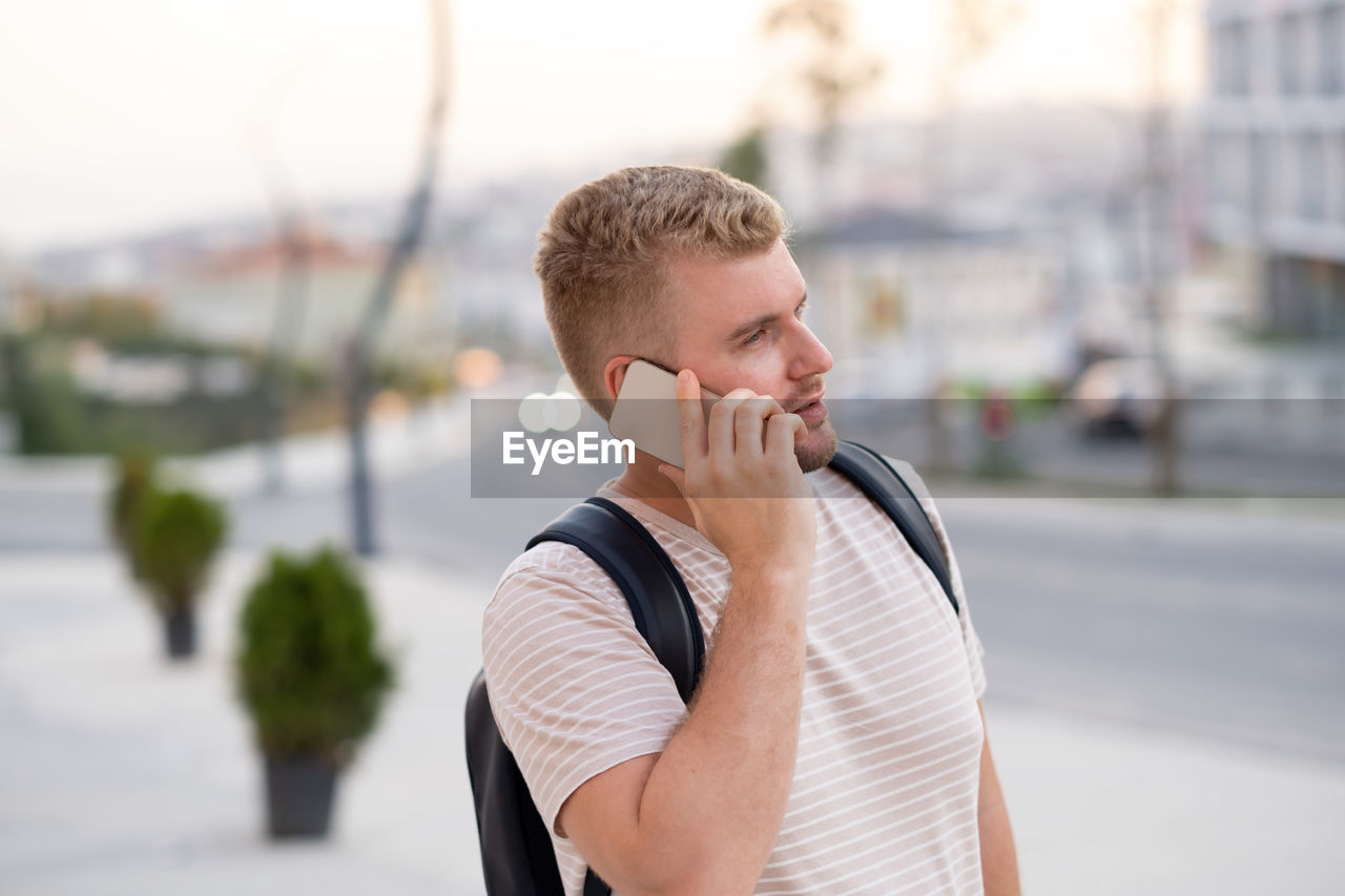 Handsome blond bearded serious man wearing backpack,casual clothes,having call using smartphone 