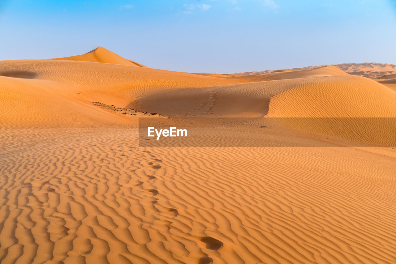 Sand dunes with footprints in them under the blue sky with soft haze on the distant horizon.