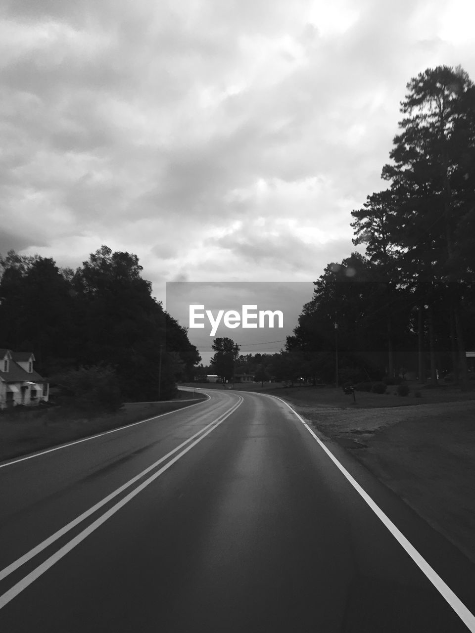 ROAD PASSING THROUGH TREES AGAINST CLOUDY SKY