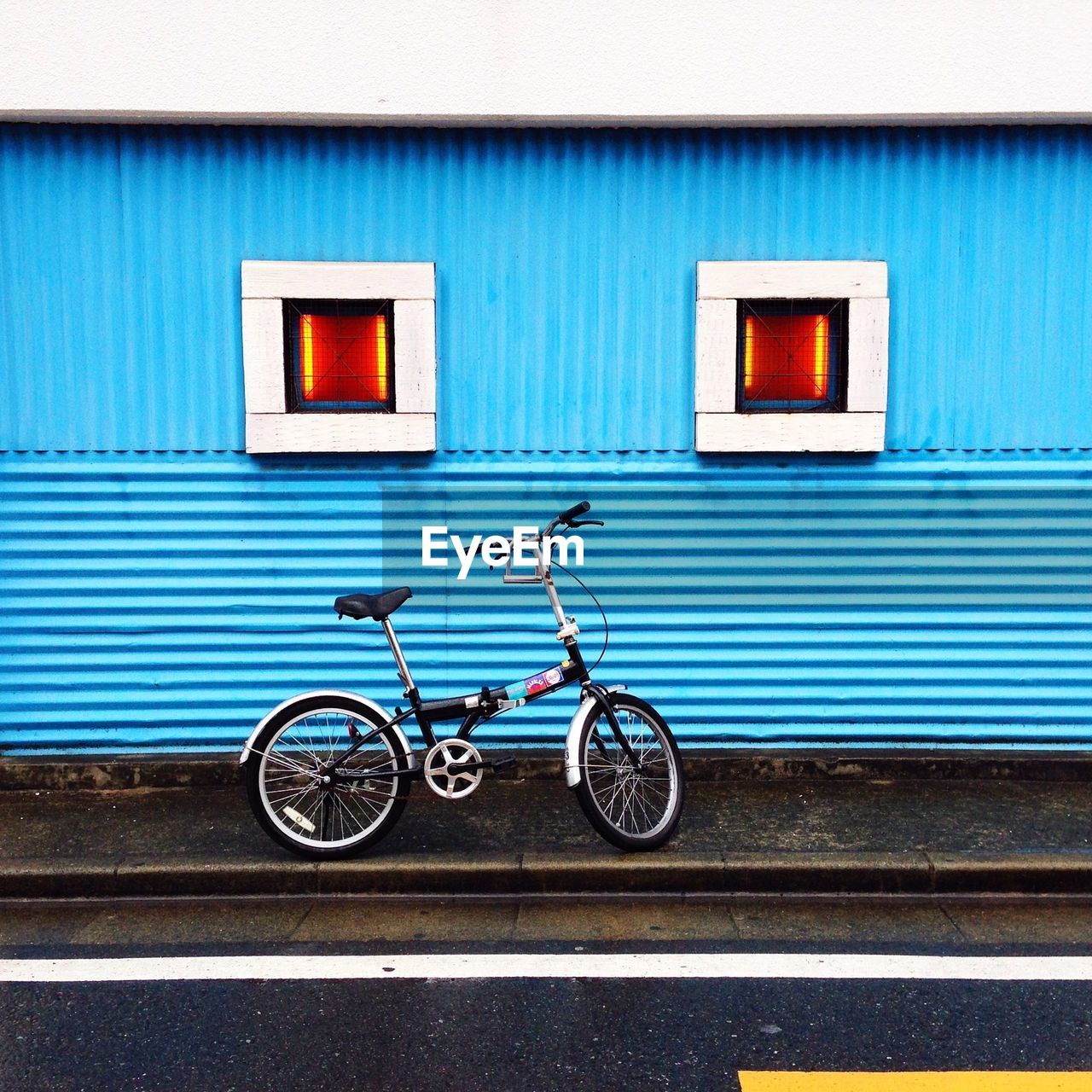 Bicycle parked against blue wall with windows