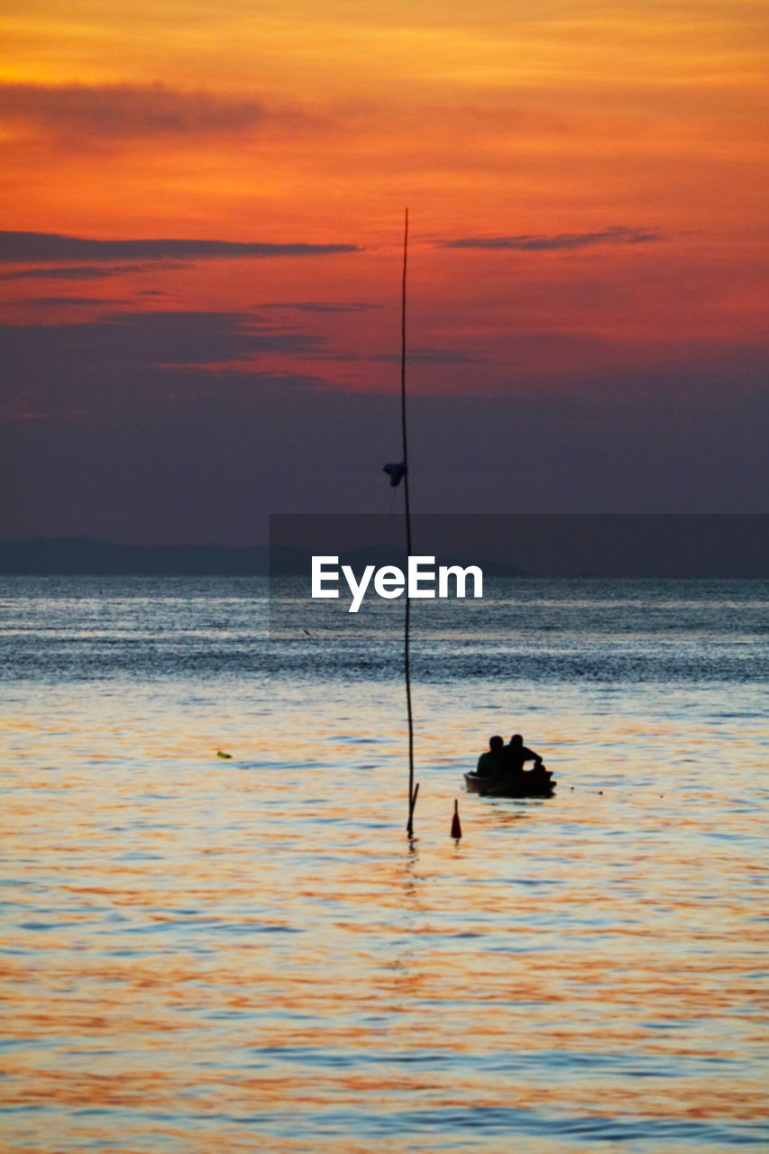 Silhouette fishing rod on sea against sky during sunset