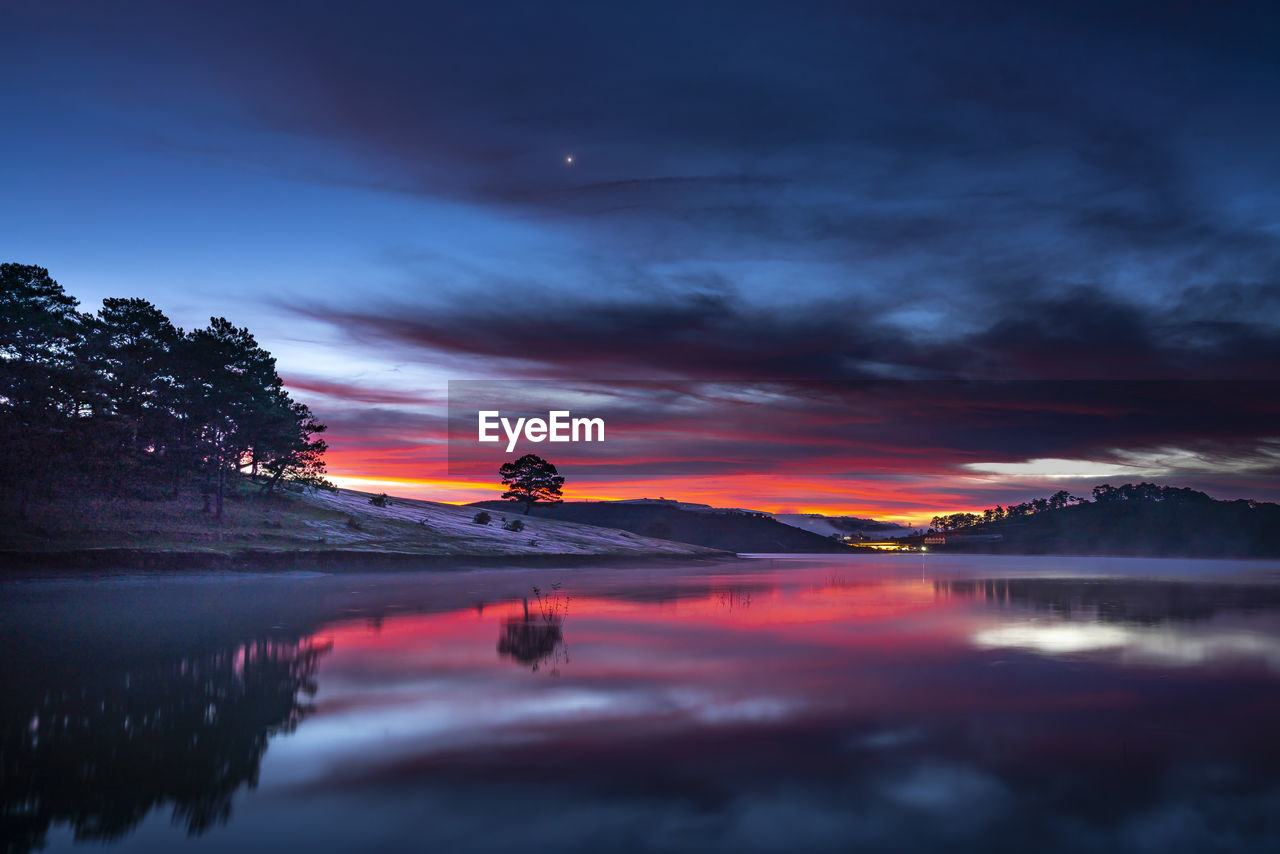 Scenic view of lake against dramatic sky during sunset