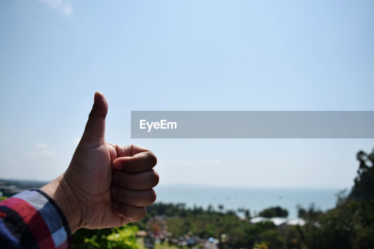 Close-up of hand showing thumbs up against clear sky