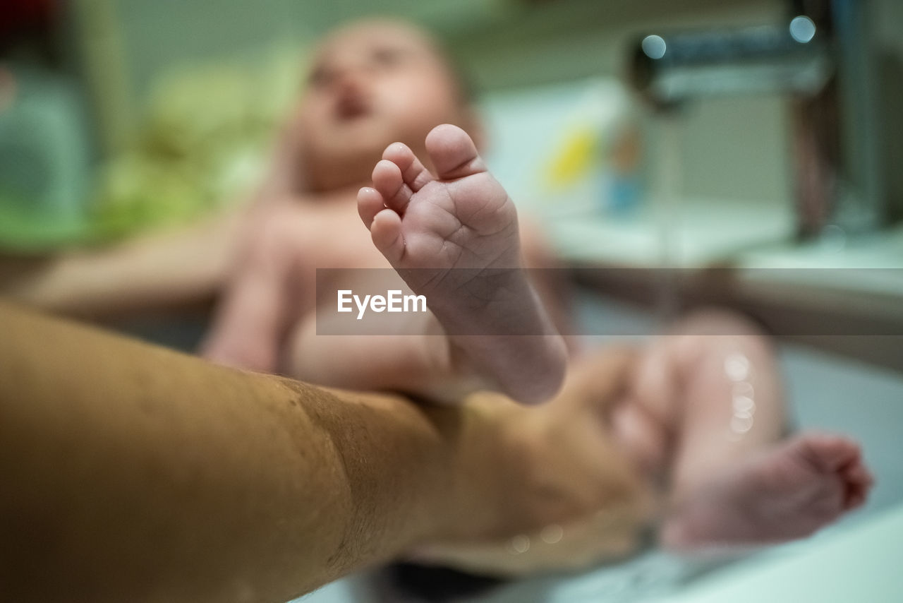 Cropped hand of mother holding baby girl in bathtub