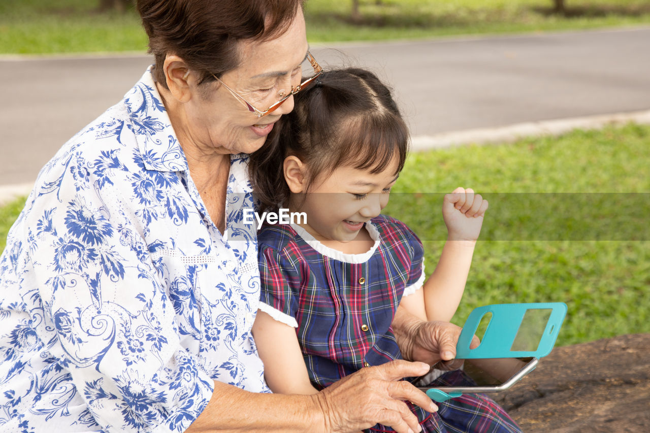 Family shot of grandmother holding her adorable granddaughter posing happily in the park outdoor 