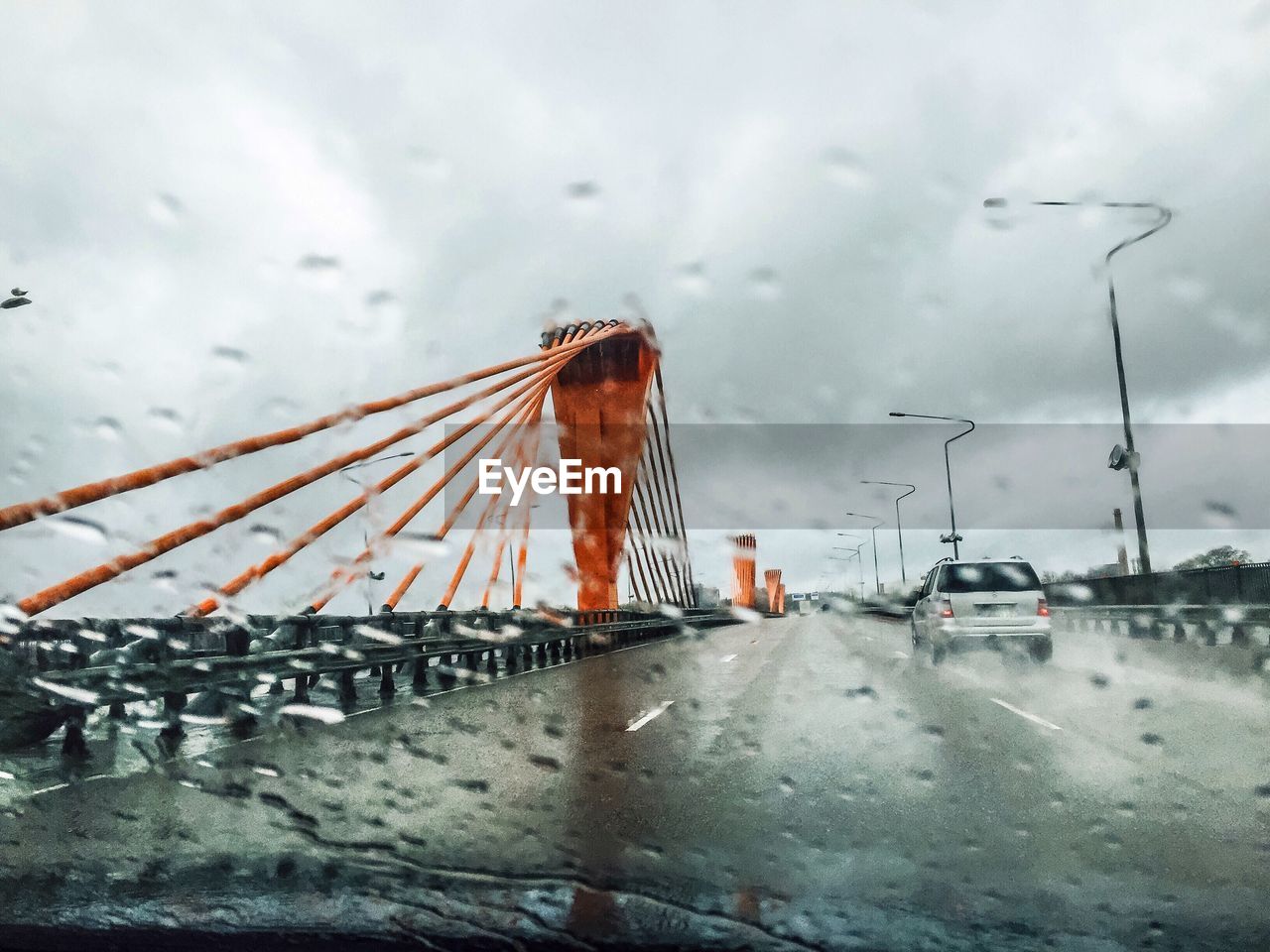 Car on bridge seen through wet windshield during rainy season