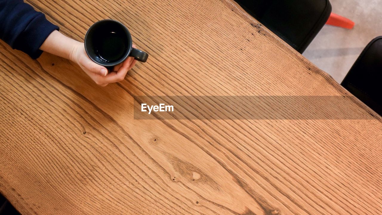 Woman holding empty coffee cup at wooden table