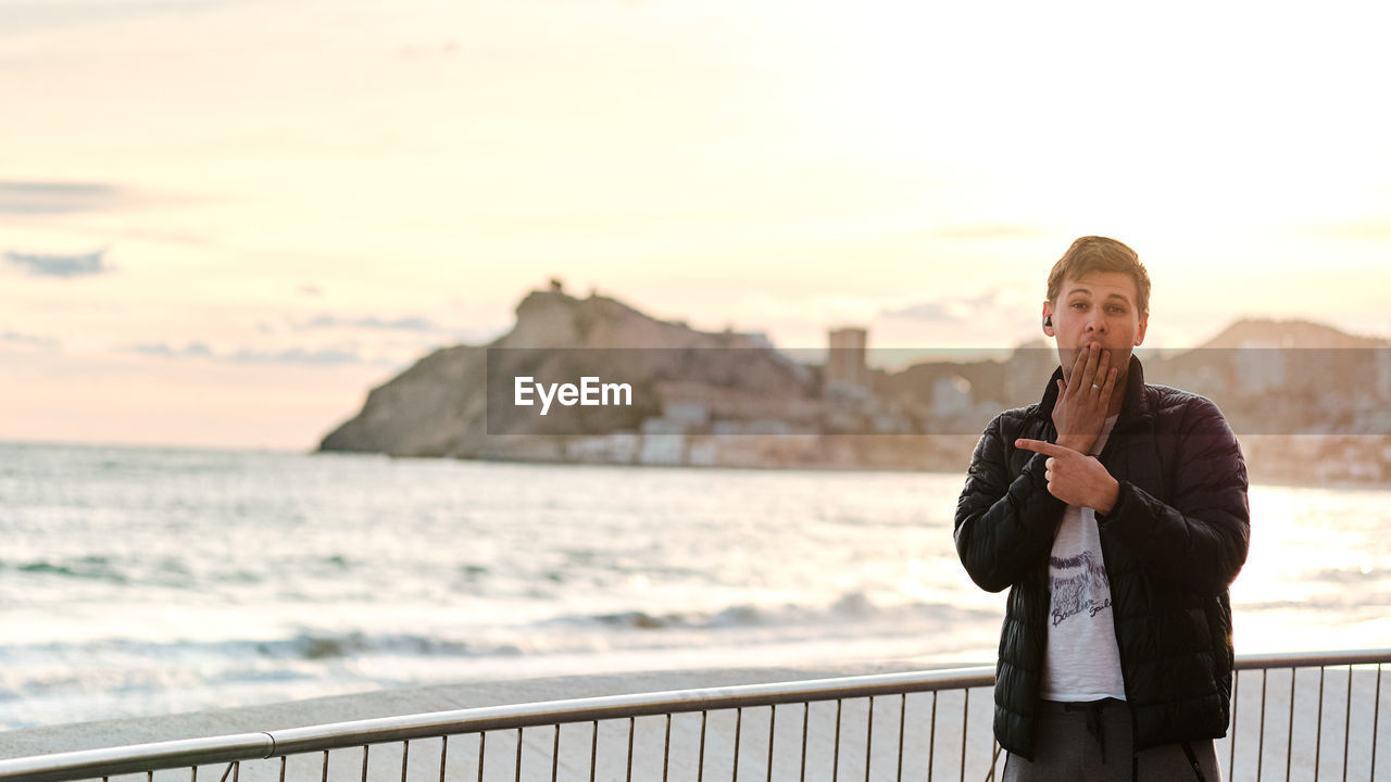 MAN STANDING BY RAILING AGAINST SEA