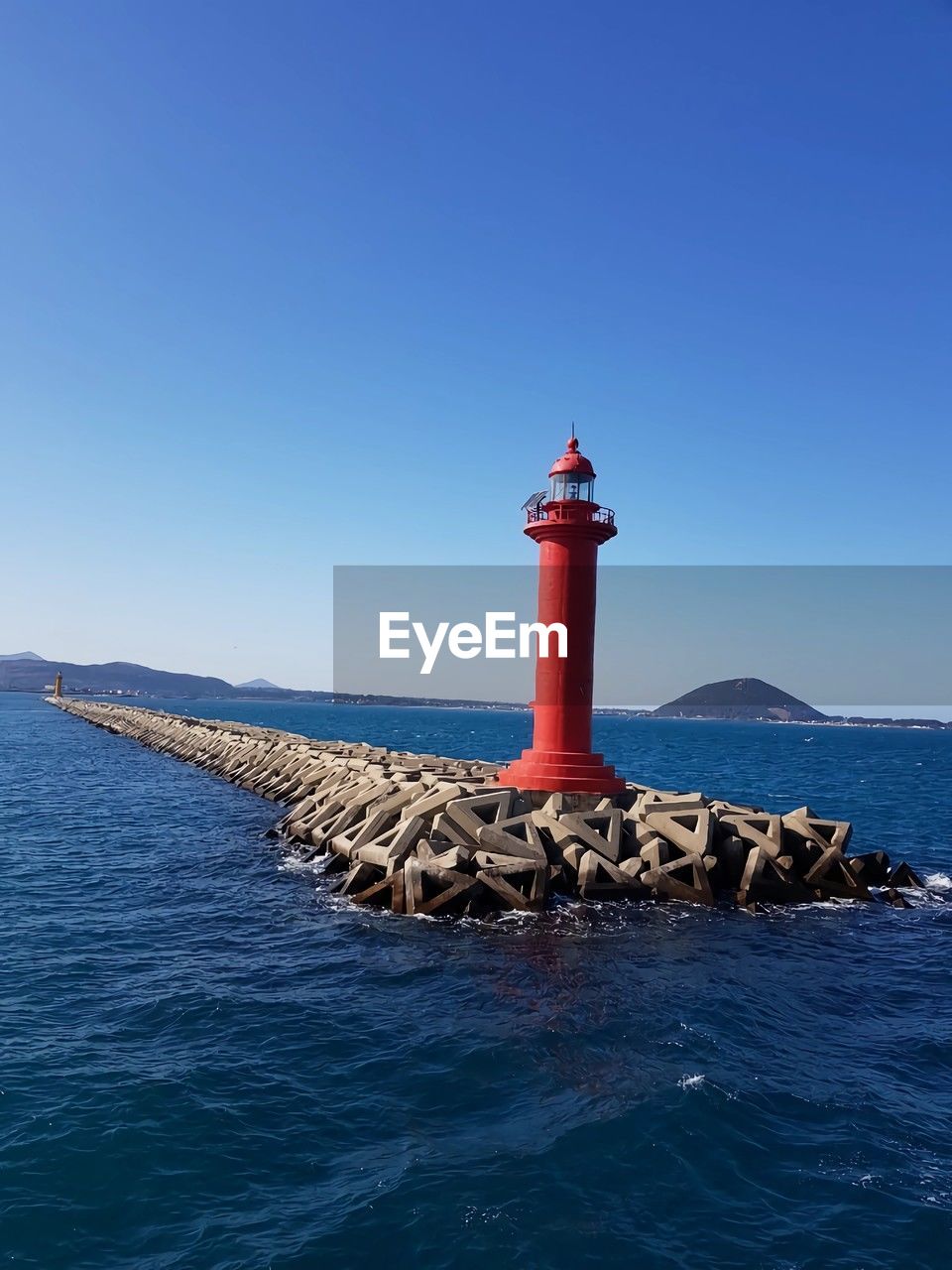 lighthouse, guidance, water, tower, sea, security, architecture, protection, built structure, sky, building, blue, building exterior, nature, ocean, coast, clear sky, no people, scenics - nature, beach, coastline, land, day, breakwater, travel destinations, outdoors, travel, beauty in nature, channel, tranquility, nautical equipment, rock, shore, landscape, transportation, non-urban scene, nautical vessel, horizon, copy space, sunny, tranquil scene, sunlight