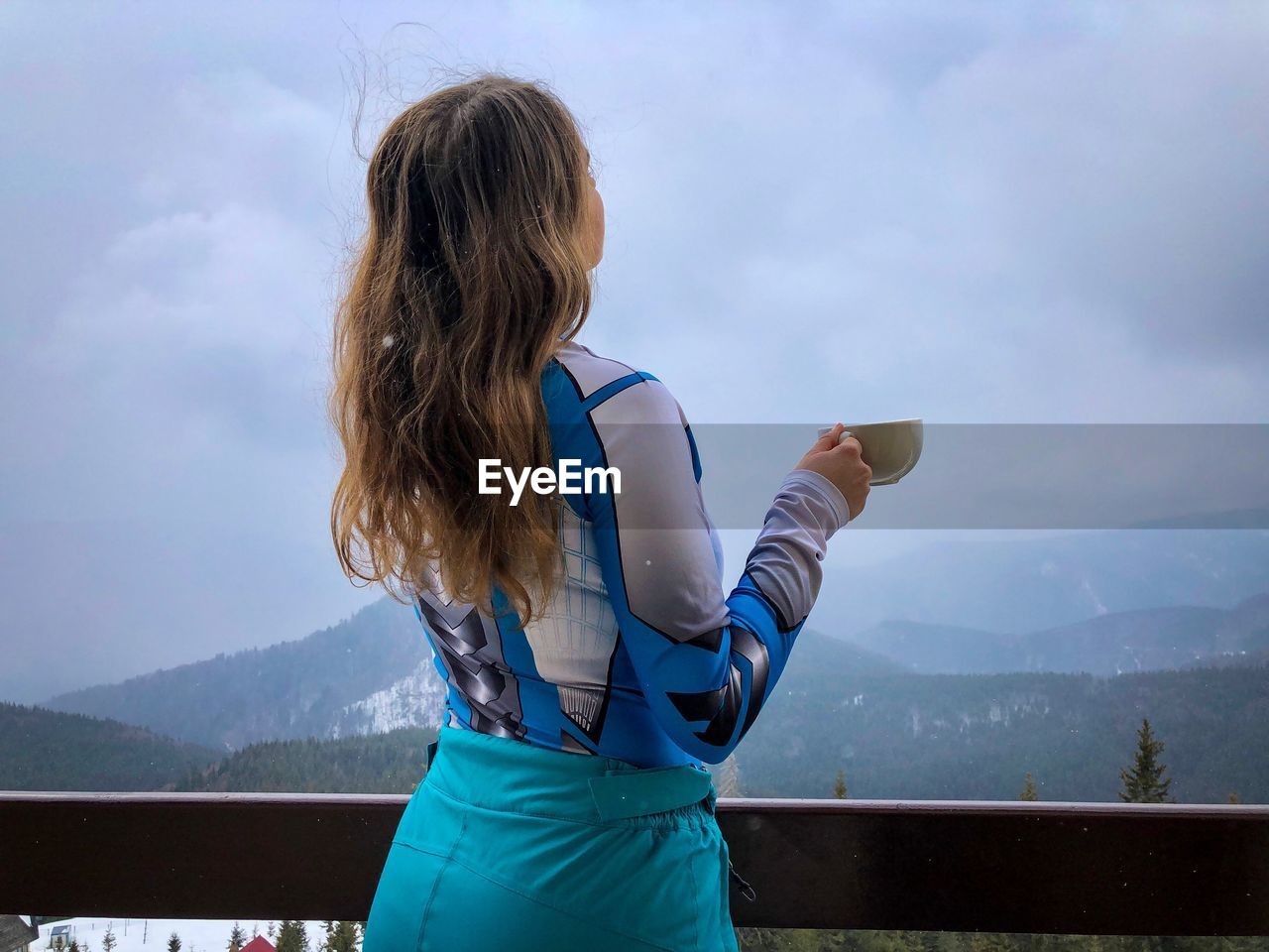 MIDSECTION OF WOMAN LOOKING AT MOUNTAINS AGAINST SKY