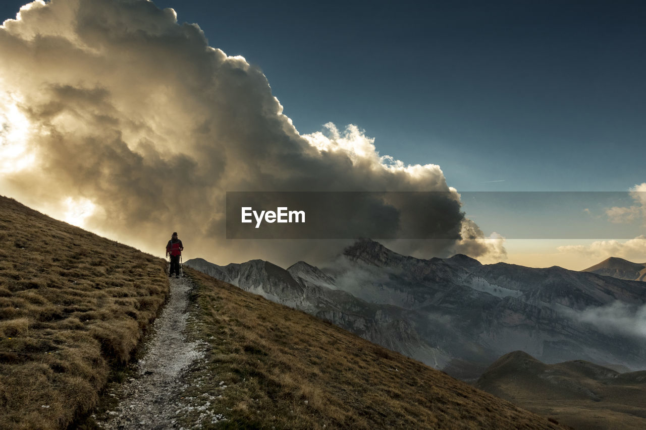 Rear view of man walking on mountain against sky during sunset