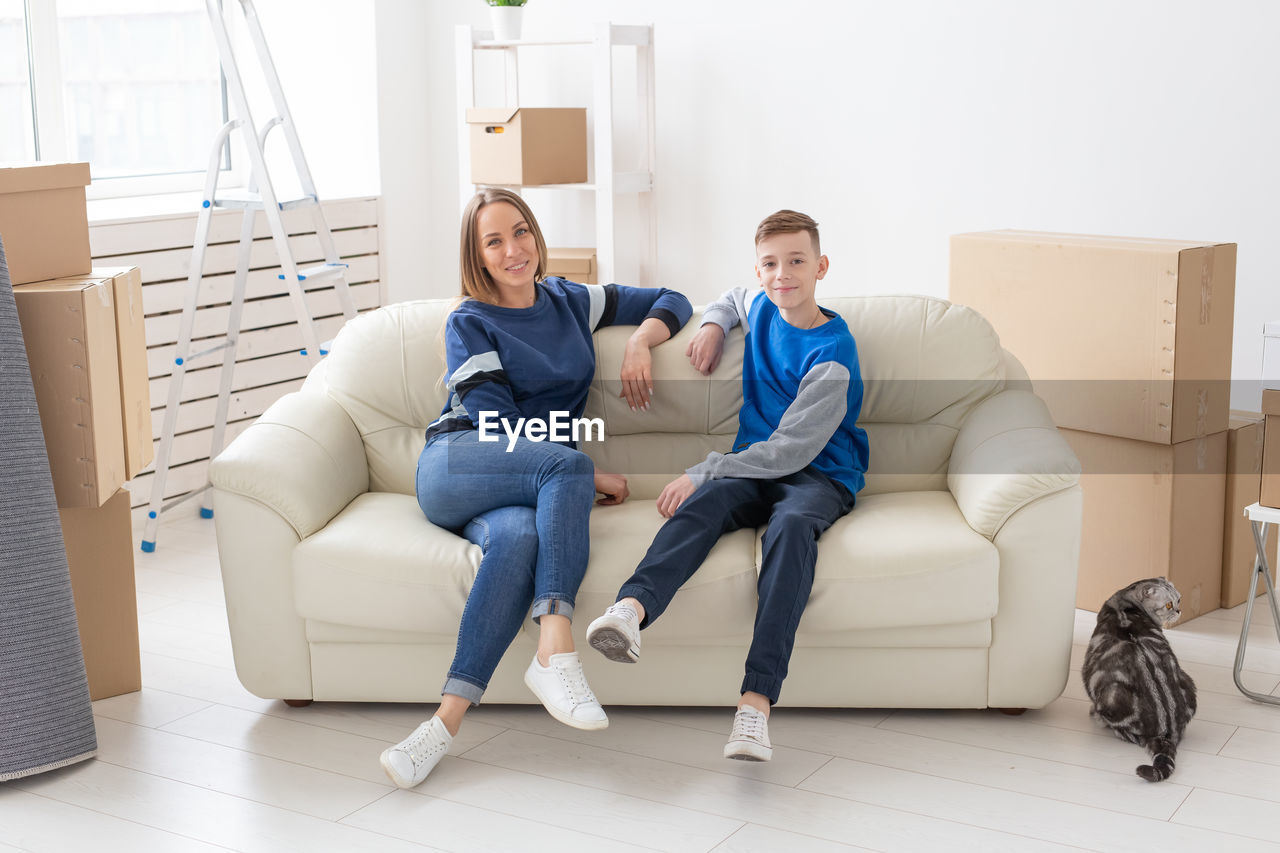 PORTRAIT OF SMILING YOUNG COUPLE SITTING ON SOFA AT HOME