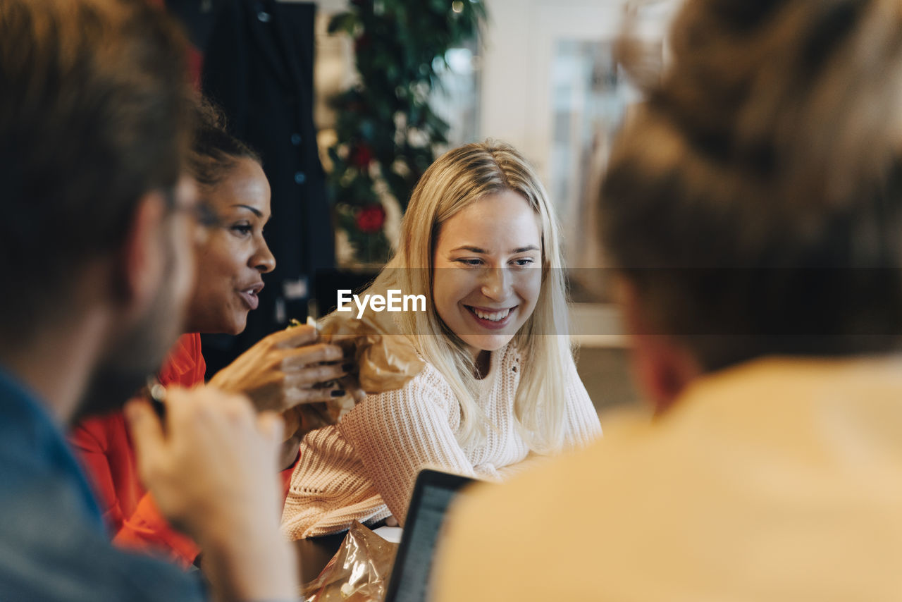 Smiling blond businesswoman sitting with mid adult colleagues during meeting at office