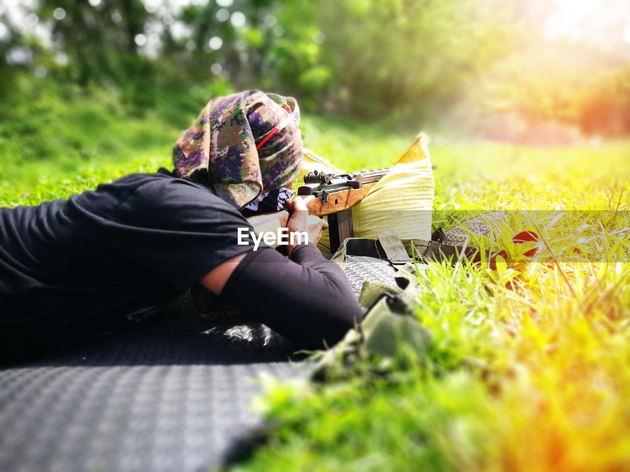 Man shooting rifle while lying on grass outdoors