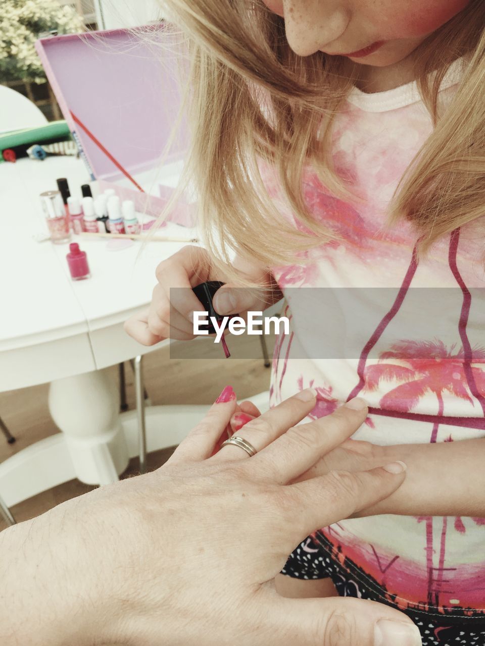 Girl applying pink nail polish on finger of woman at home