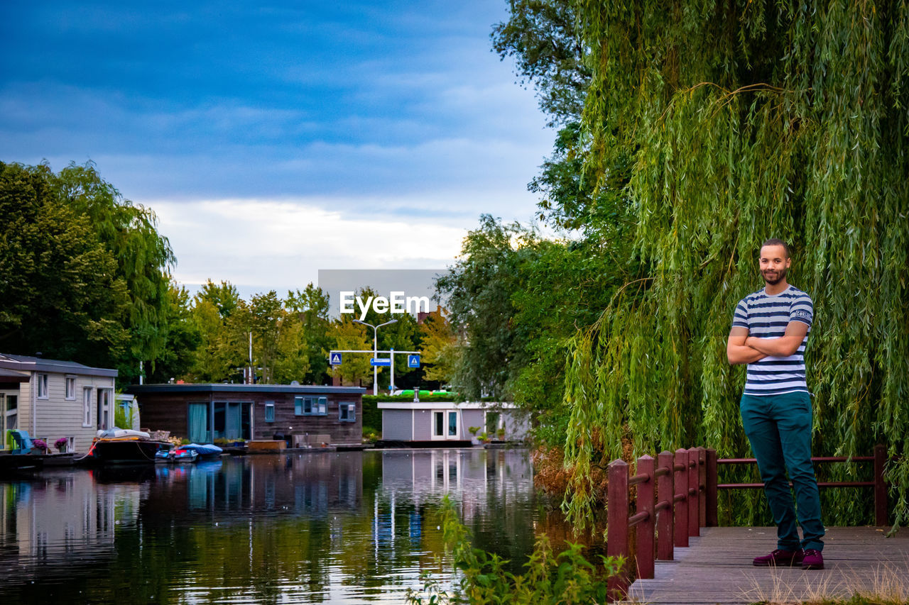 Portrait of man standing by lake against trees