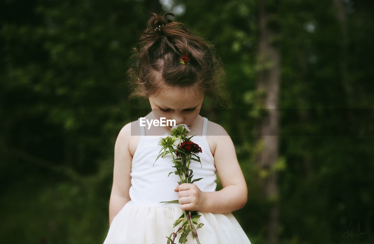 Girl holding flower against trees