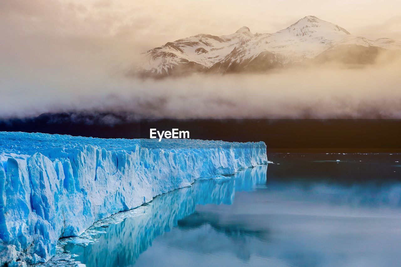 Scenic view of iceberg in water against snowcapped mountains during winter