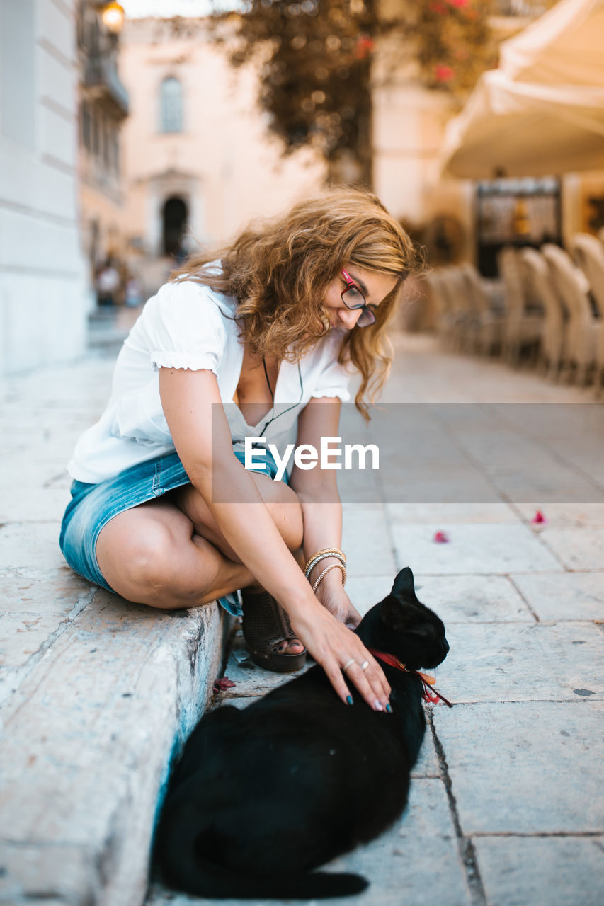 Smiling woman with black cat on footpath in city