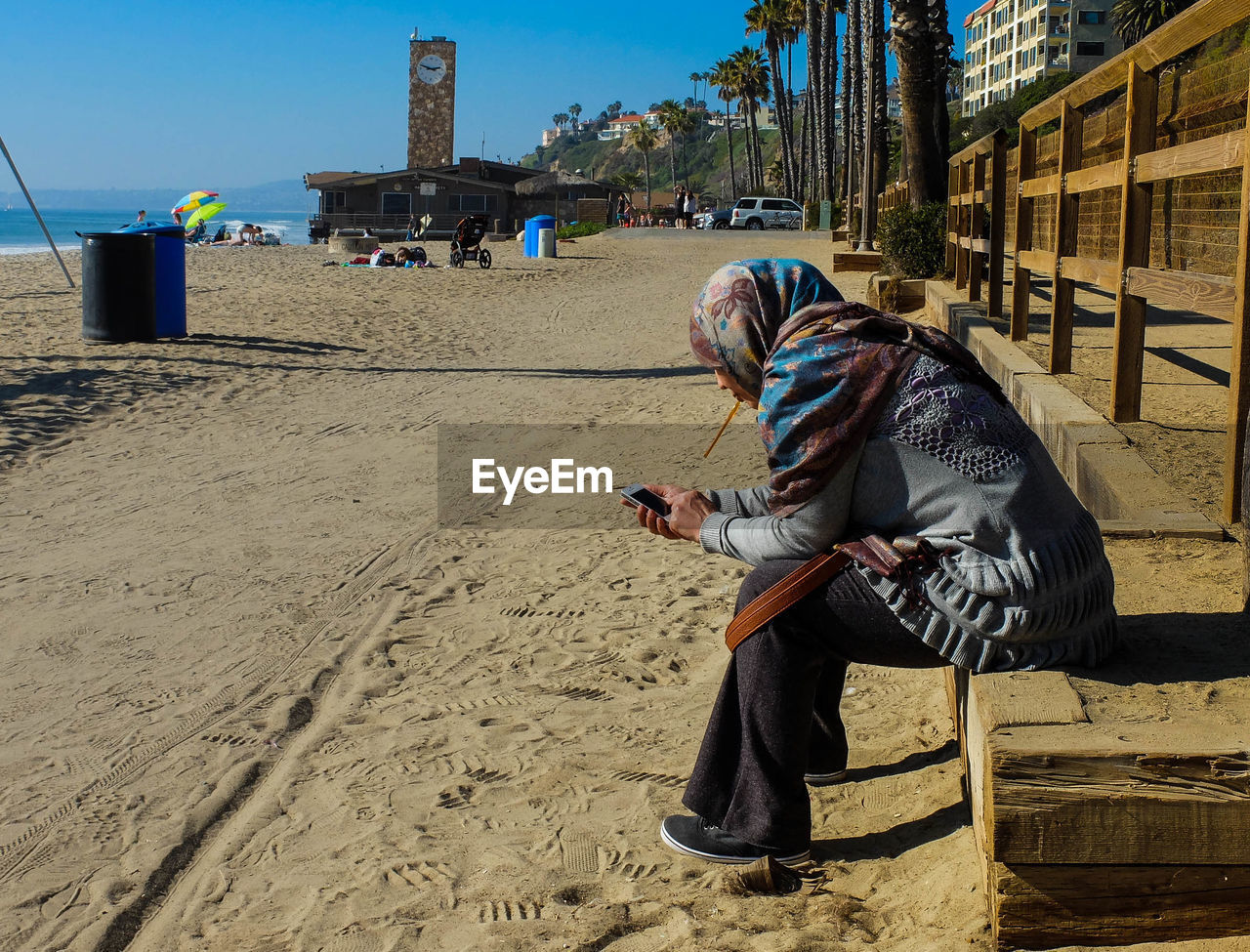 Woman wearing hijab using cell phone at beach