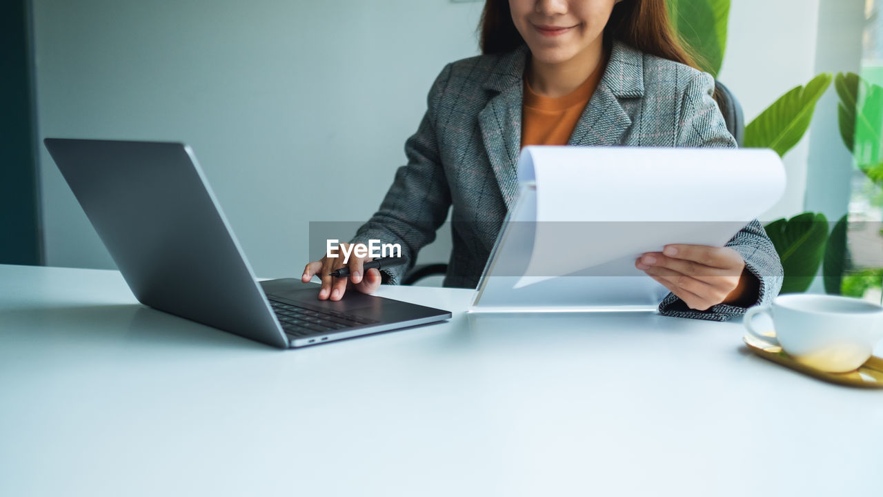 midsection of businesswoman using laptop while sitting on table