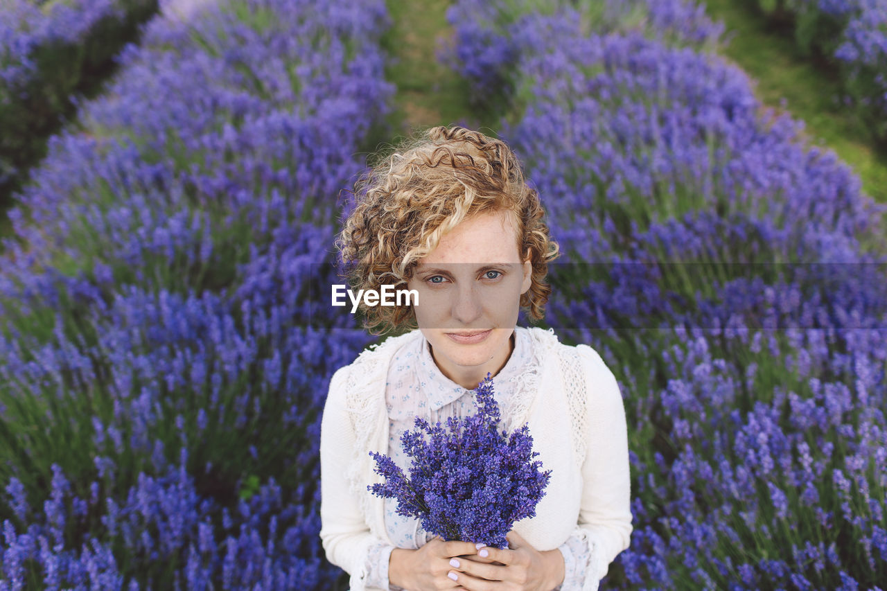 Portrait of woman holding lavenders while standing on field