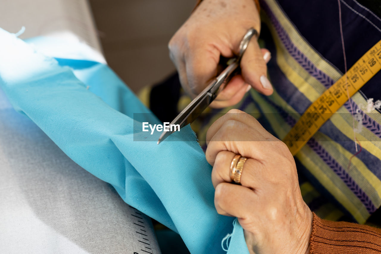 Detail of senior dressmaker hands cutting fabric with scissors.