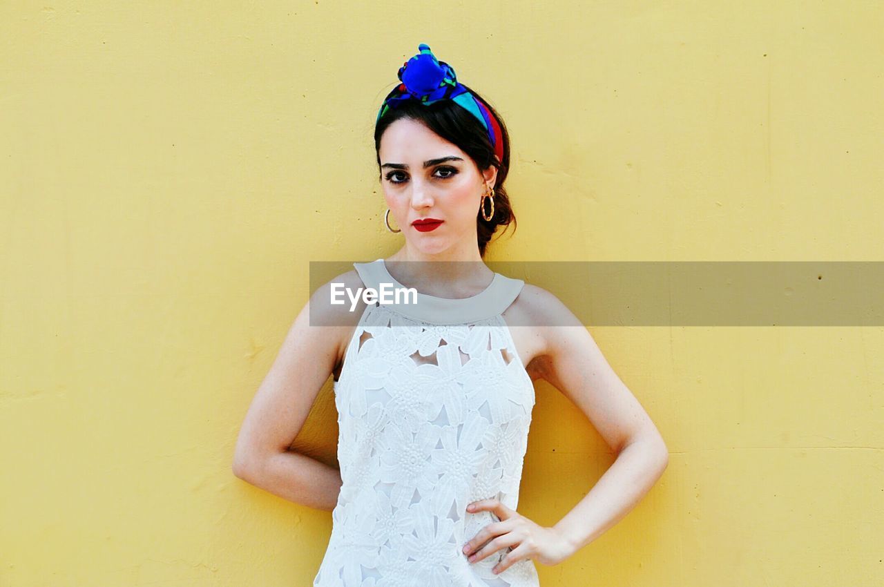Portrait of beautiful young woman standing against yellow wall