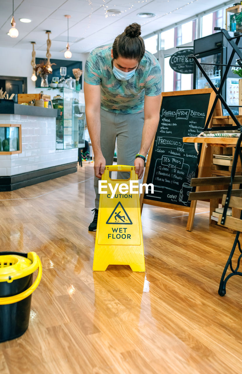 Waiter wearing mask putting warning sign in cafe