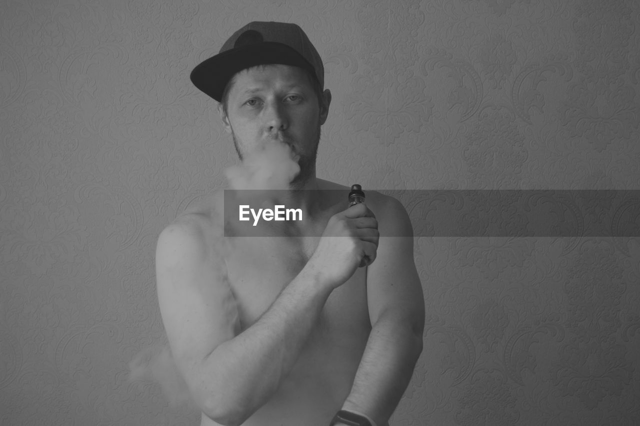 Portrait of young man smoking against wall